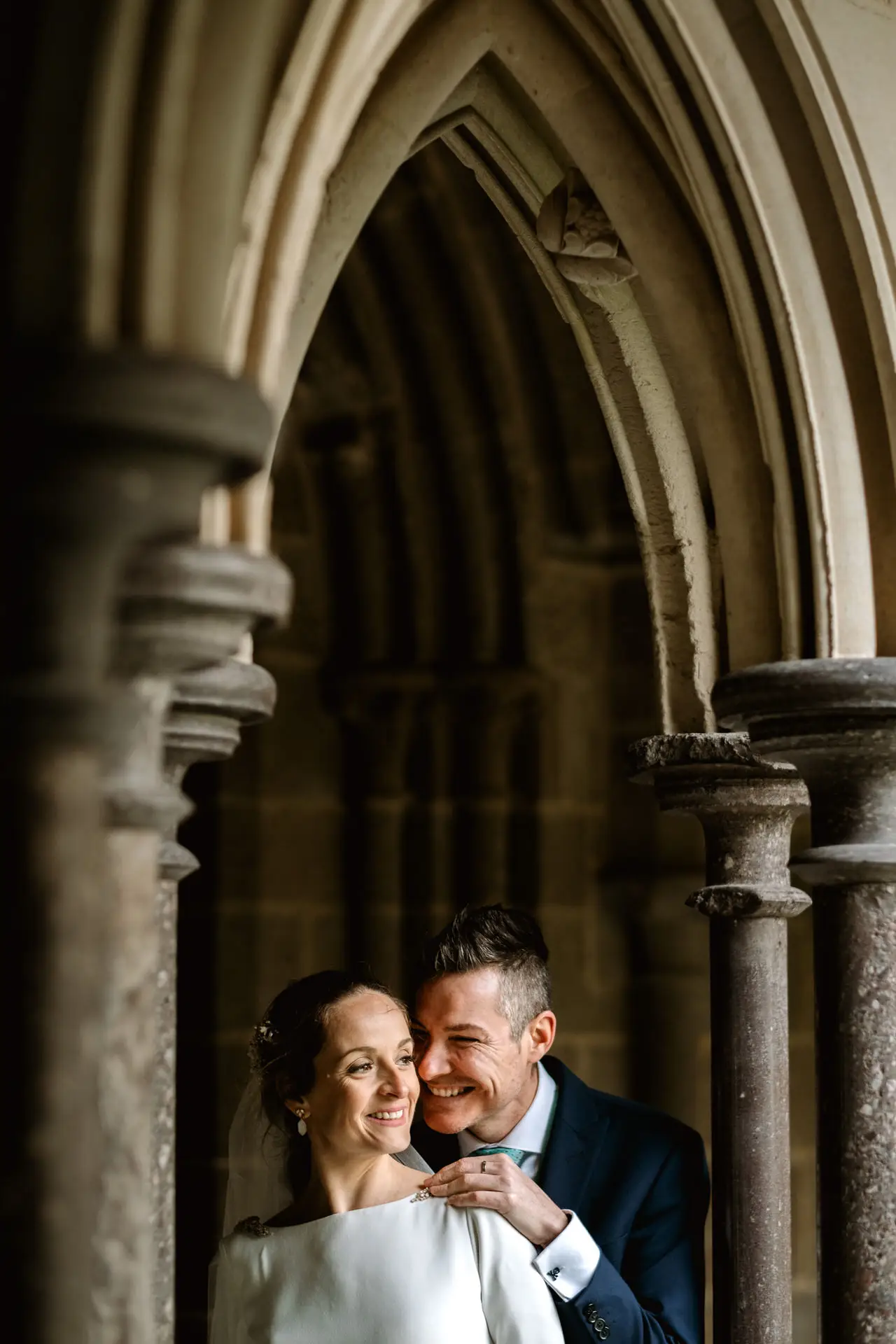 Los novios sonríen bajo un arco gótico de la abadía, en su postboda en Francia