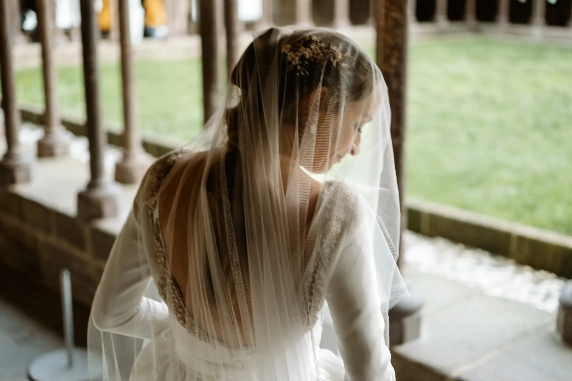 Detalle de la espalda y el velo de la novia junto al jardín del claustro, en su postboda en Francia