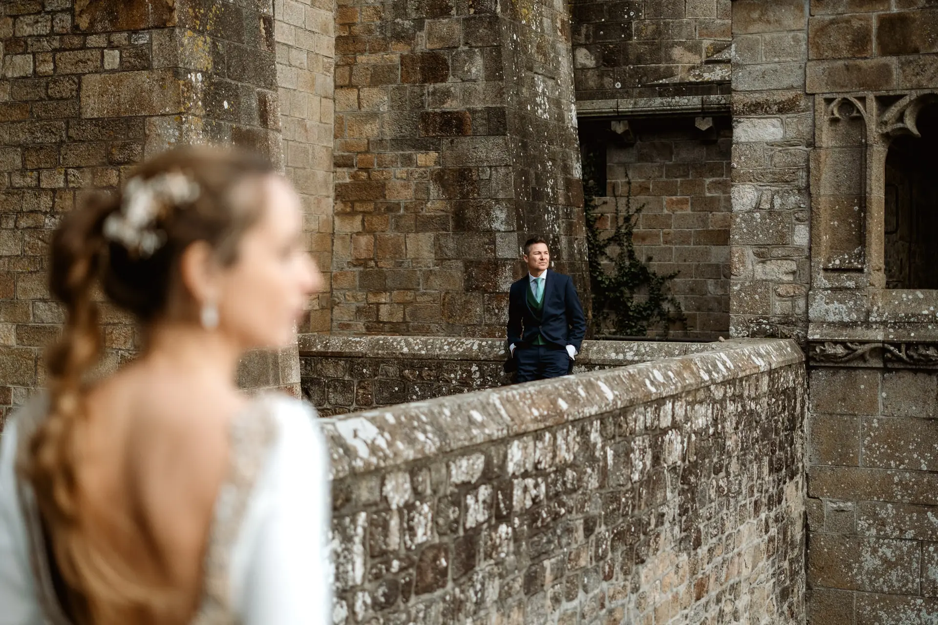 La novia en primer plano y el novio al fondo sobre la muralla, en su postboda en Francia