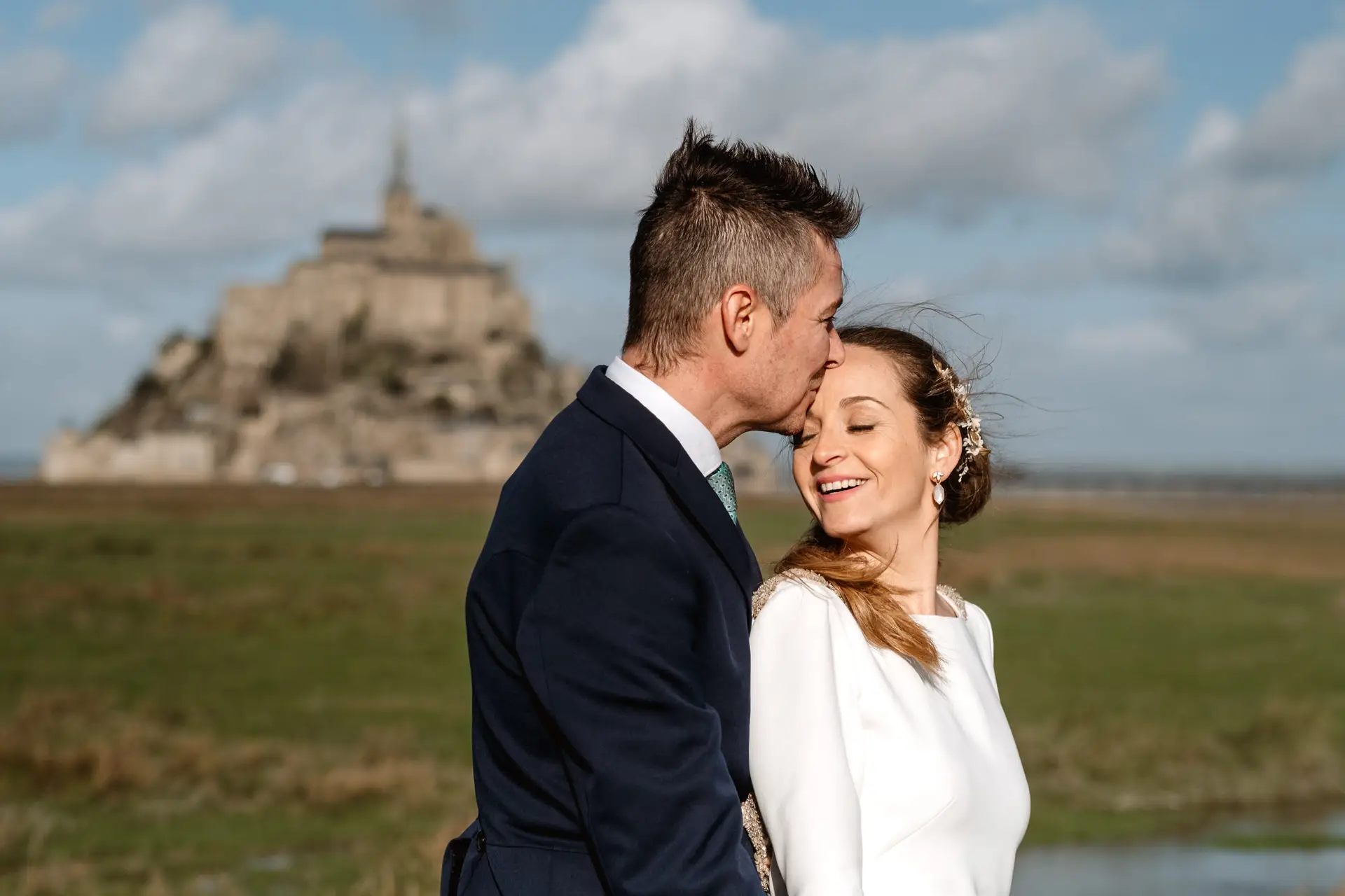 El novio besa la frente de la novia ante el Mont Saint-Michel