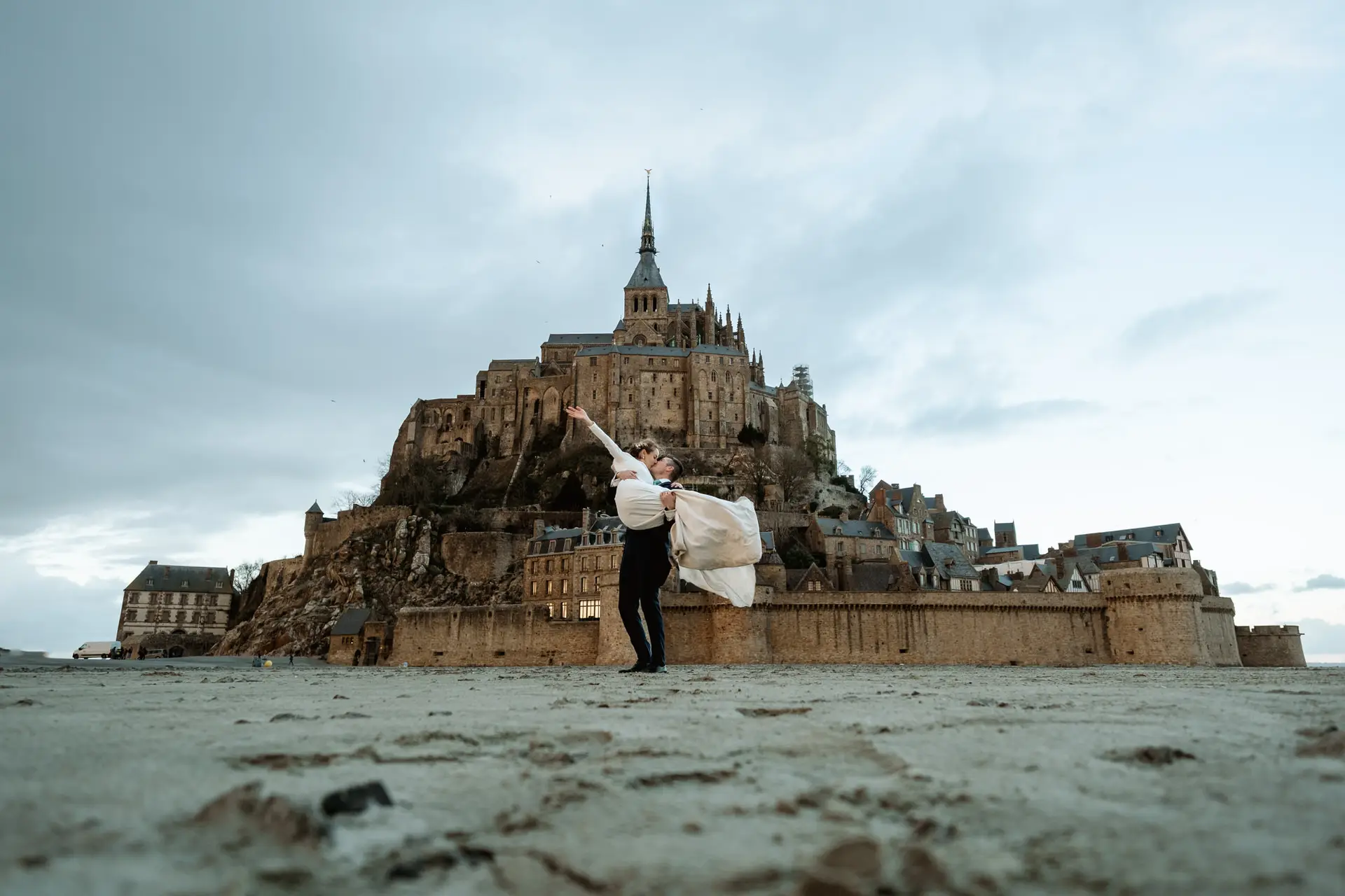El novio levanta a la novia en la playa ante el Mont Saint-Michel