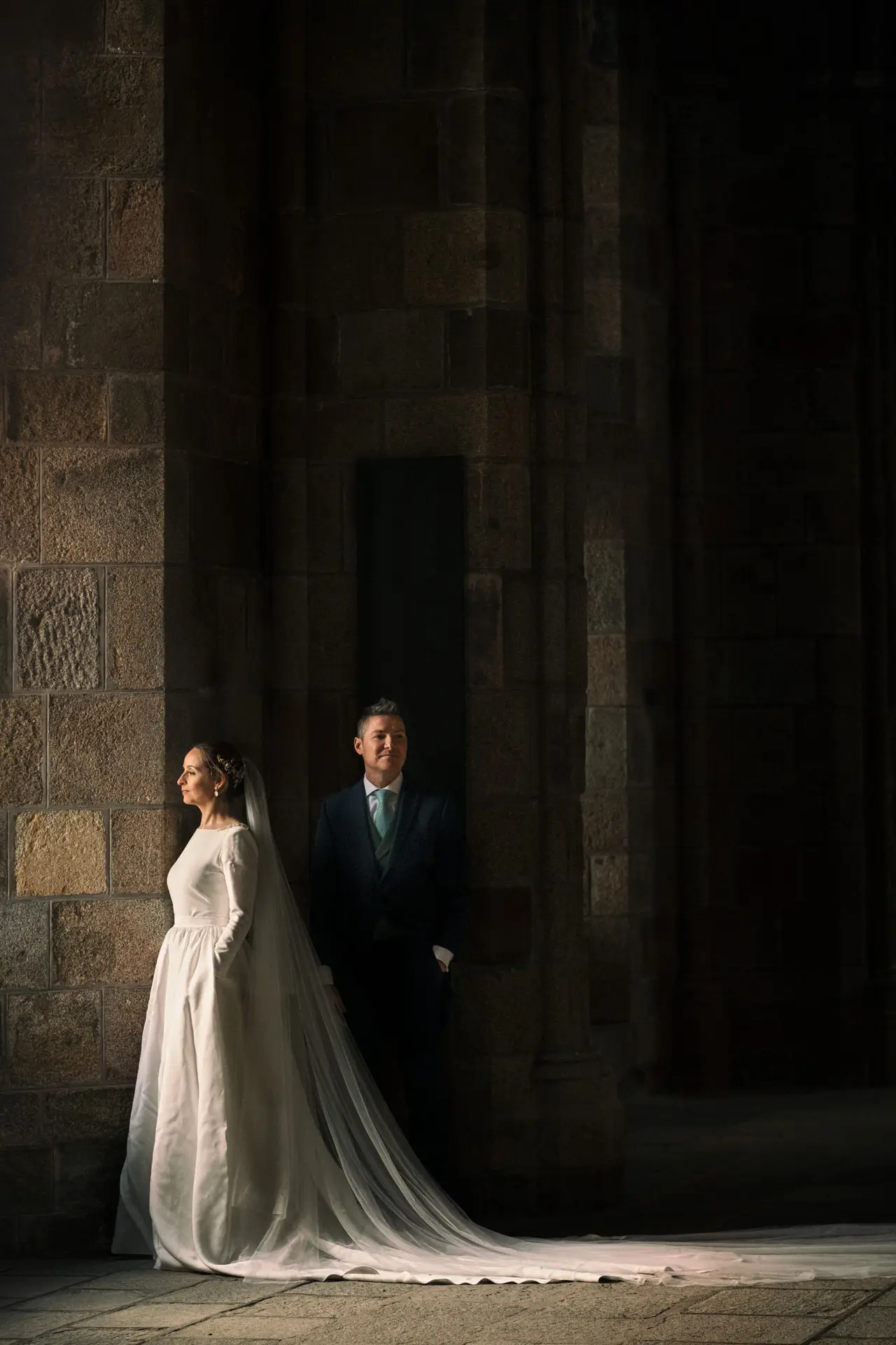Los novios con el velo largo en un pórtico de piedra, en su postboda en Francia