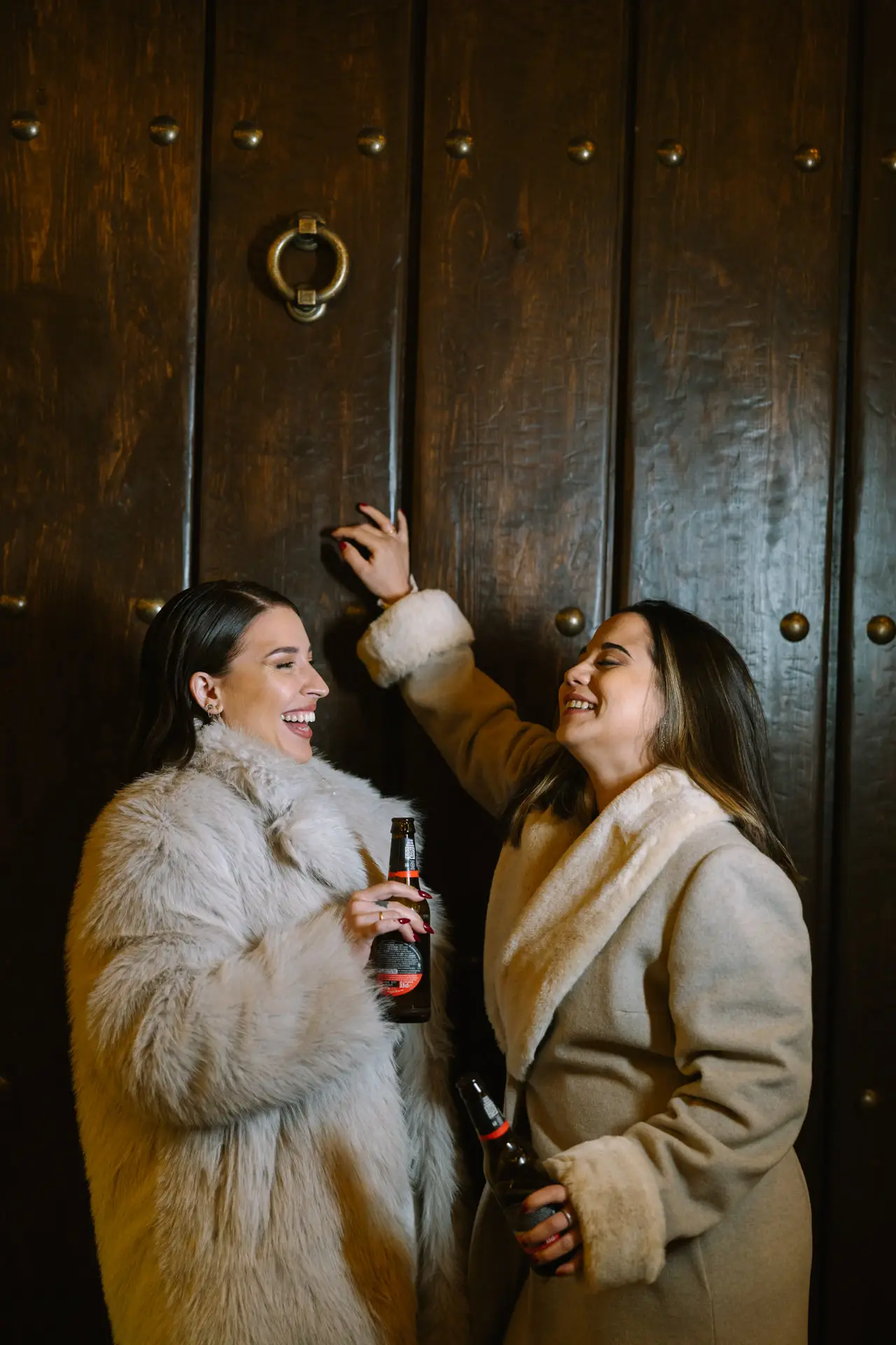 Rocío y Nines brindan con cerveza ante una puerta antigua, en Badajoz