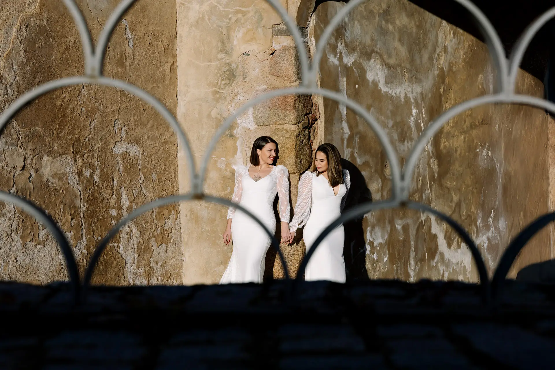 Rocío y Nines tras una reja de hierro junto a un muro antiguo, en Badajoz
