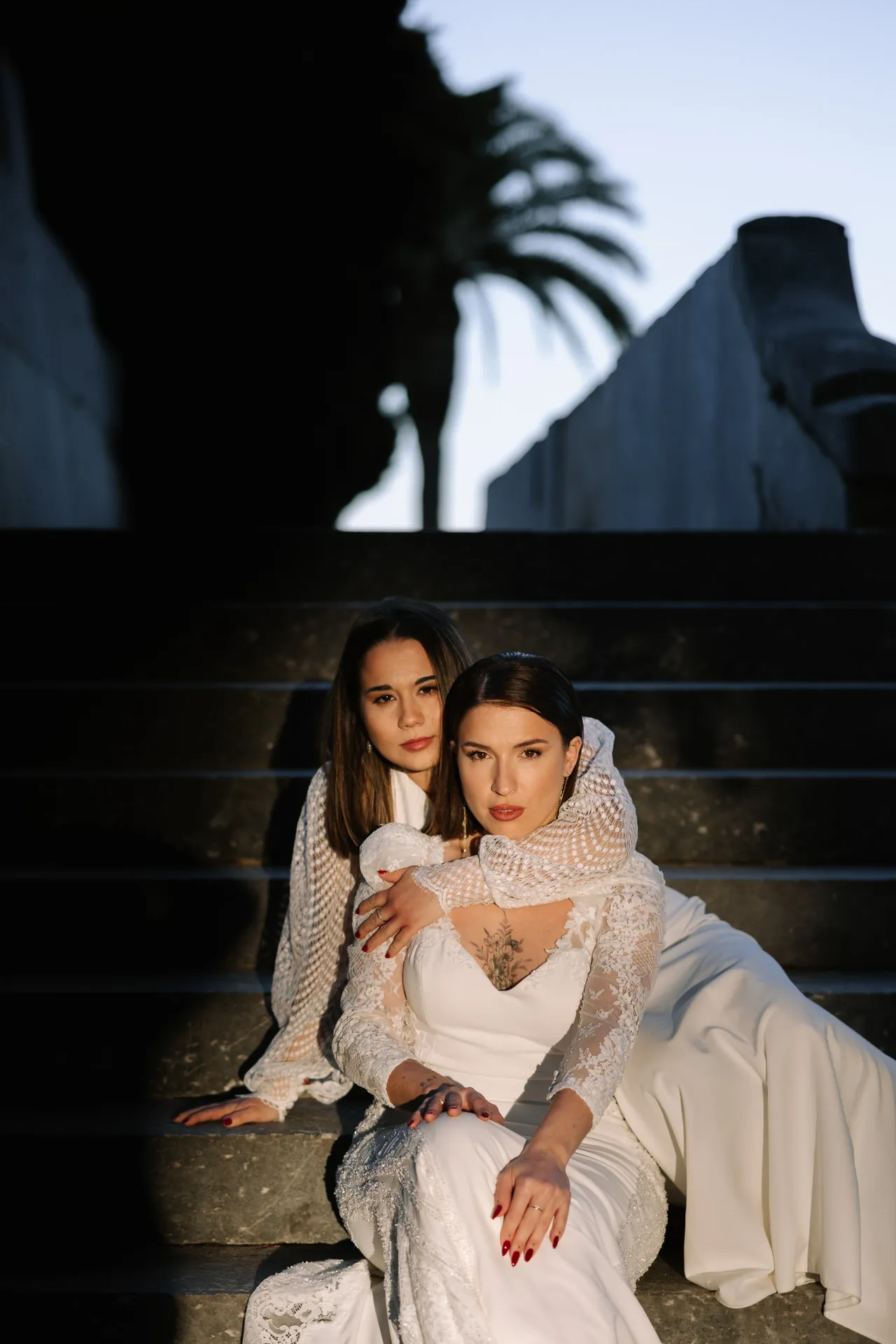 Rocío y Nines abrazadas en unas escaleras al atardecer en su postboda de Navidad en Badajoz
