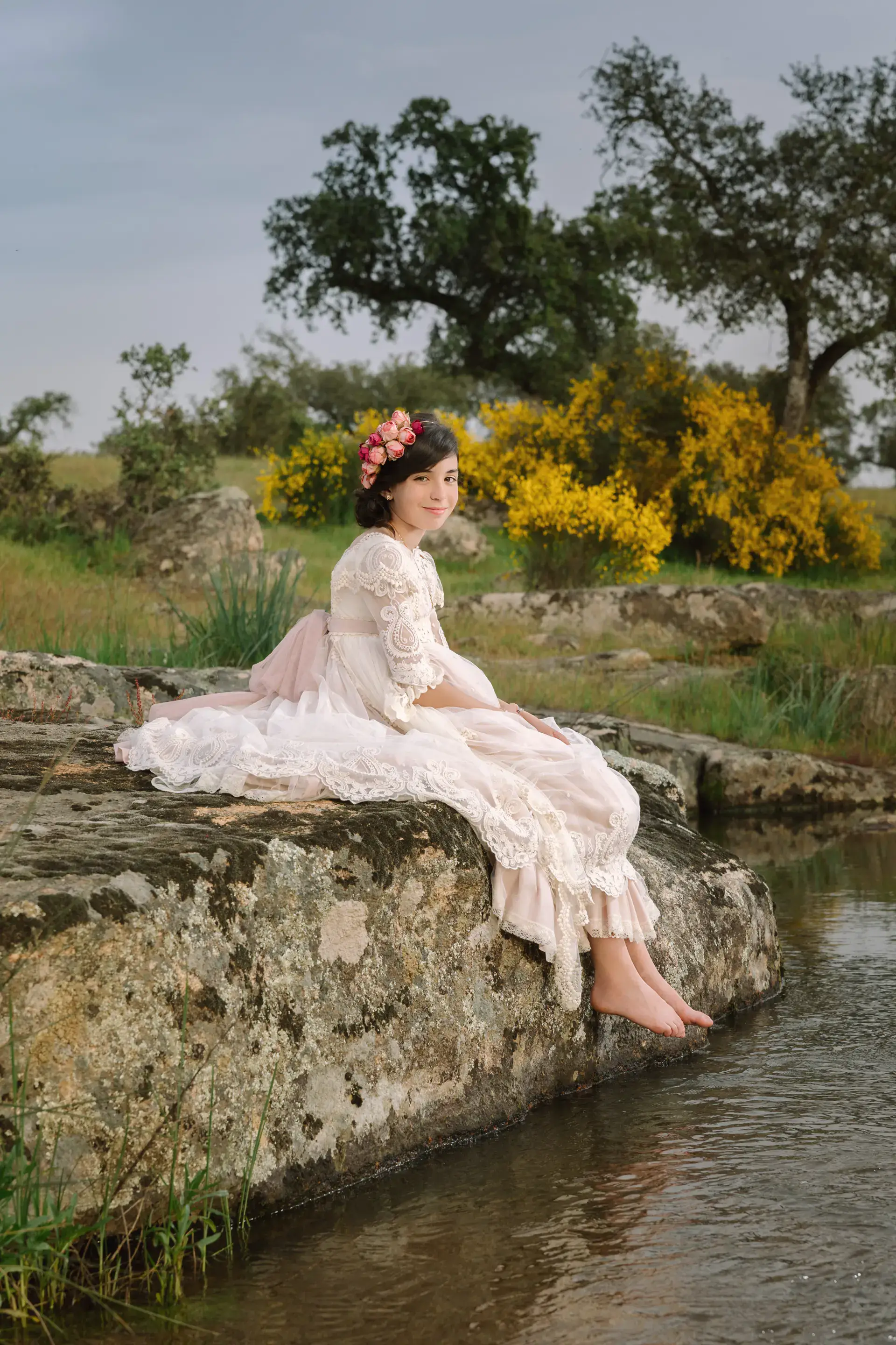 Niña con vestido de comunión rosa sentada en una roca junto a un arroyo