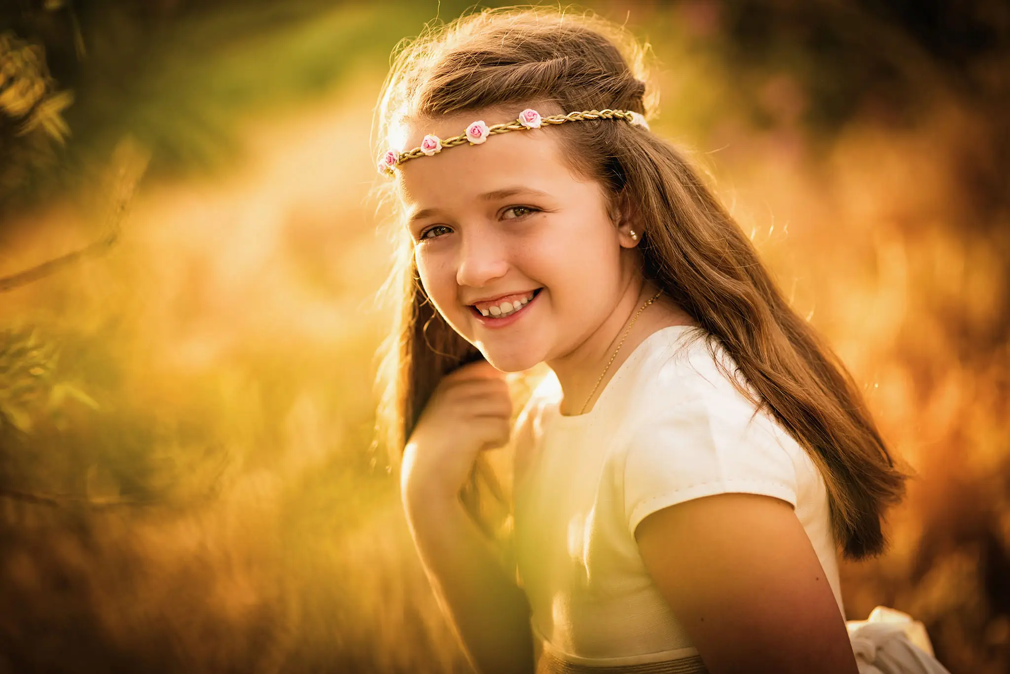Niña con diadema de flores sonríe a contraluz al atardecer